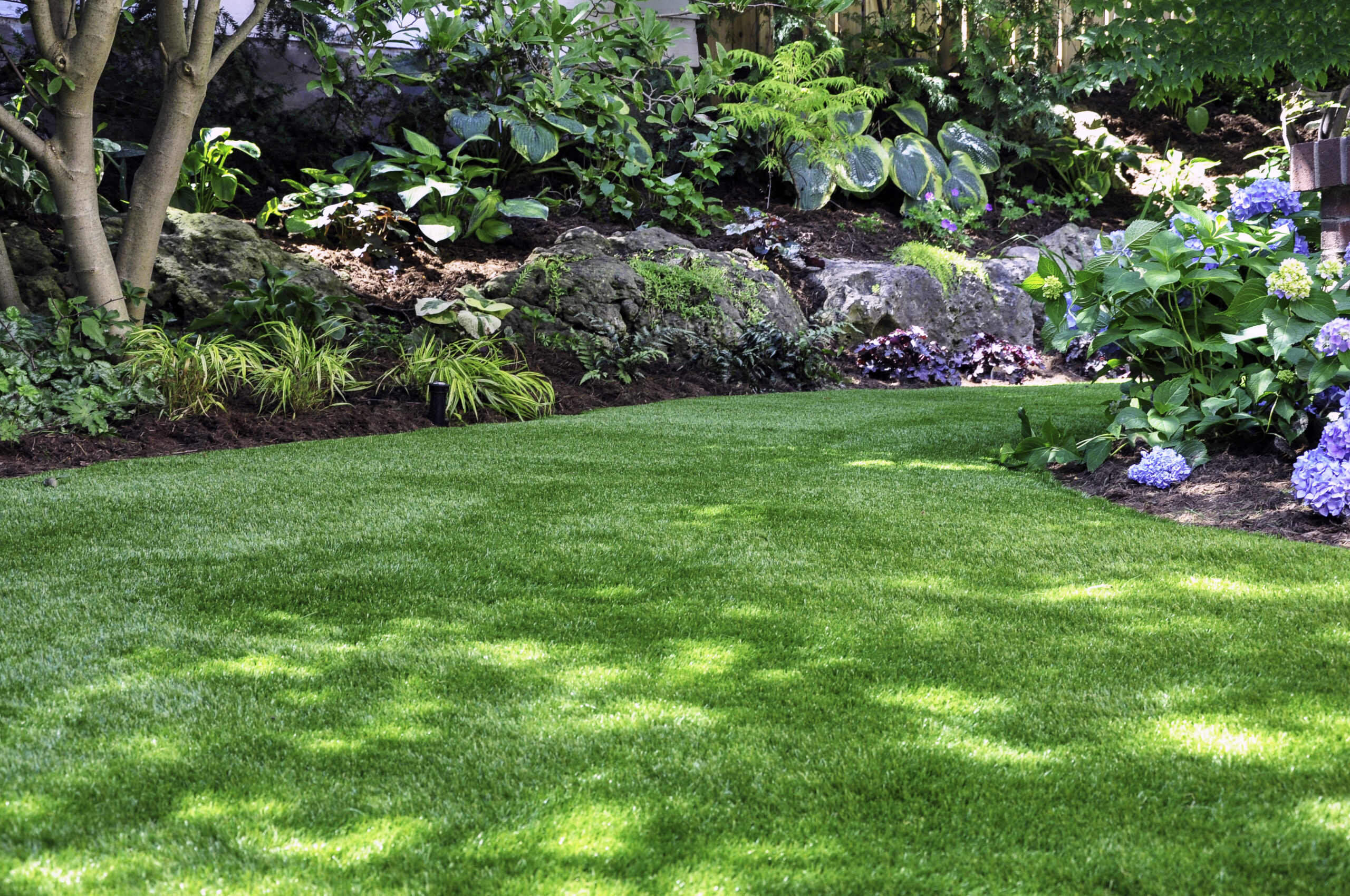 This beautiful backyard woodland garden features a maintenance free lawn made of natural looking artificial grass, a huge landscaping trend for small spaces.